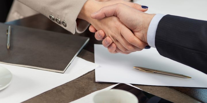 We made a deal. Close up of arms of successful two business partners shaking hands. They are sitting at the table near documents in cafe. The businessman and woman are drinking coffee